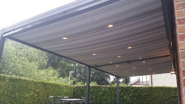 Eine überdachte Terrasse mit gestreiftem Vordach und eingebauter Beleuchtung, die an eine Backsteinmauer angebaut ist.