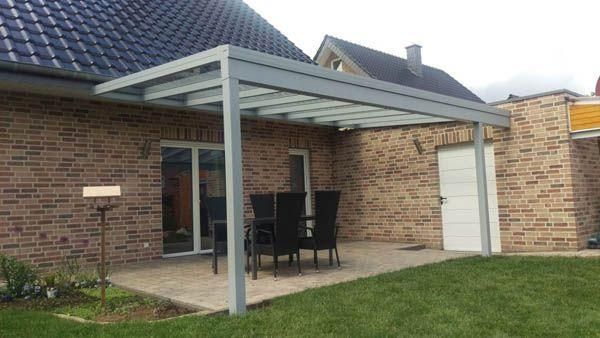 Terrasse mit Metallmarkise, Tisch und Stühlen an einem Backsteinhaus mit Tür und Rasen.