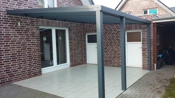 Grau überdachte Terrasse an einem Backsteingebäude; weiße Türen, Fliesenboden.