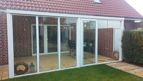 Wintergarten an einem Backsteinhaus mit großen Glasfenstern und -türen.