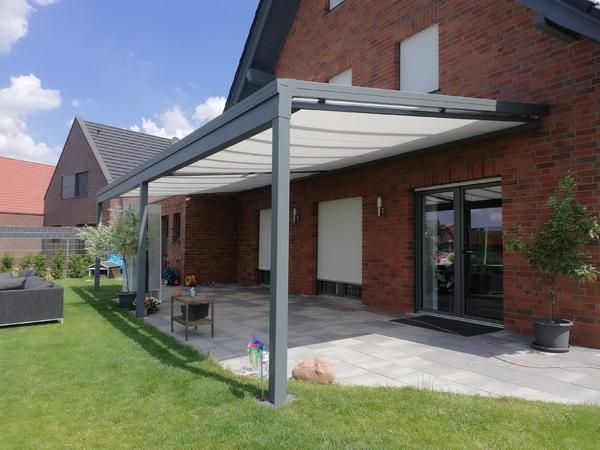Eine Terrasse mit weißem Vordach an einem Backsteinhaus an einem sonnigen Tag.