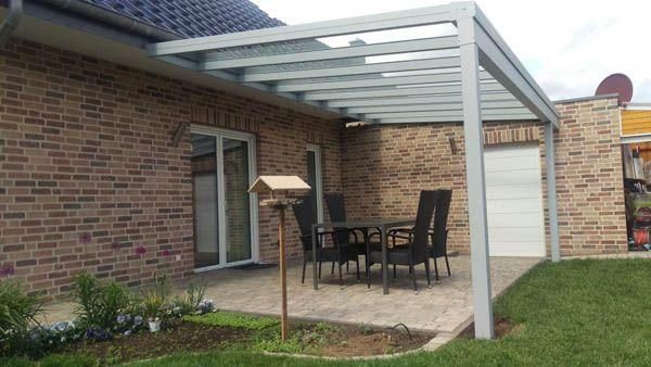 Terrasse mit Tisch und Stühlen unter einer Metallpergola, die an ein Backsteinhaus angebaut ist.
