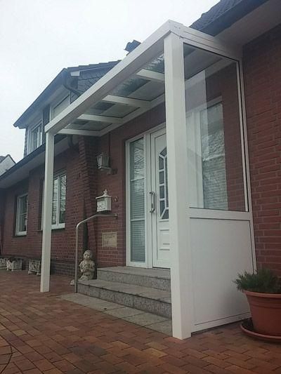 Weißes Vordach über dem Eingang eines Backsteinhauses mit Treppe, weißer Tür und einer Topfpflanze.