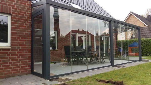 Ein verglaster Wintergarten, der an ein Backsteinhaus angebaut ist und in dem ein Esstisch mit Stühlen sichtbar ist; befindet sich auf einem Rasen.