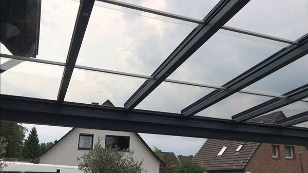 Glasdachkonstruktion über den Fenstern eines Gebäudes, sichtbarer Himmel, schwarze Balken, bewölkter Tag.