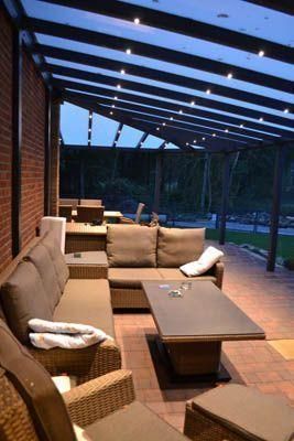 Sitzbereich im Freien mit Sofa, Tisch und Deckenbeleuchtung unter einem transparenten Dach.