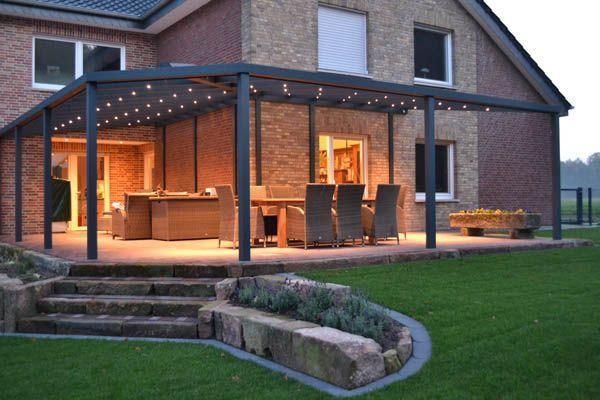 Terrasse mit Pergola, Gartenmöbeln und Backsteinhaus, beleuchtet von Lichterketten.
