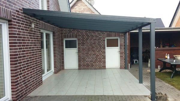 Überdachte Terrasse mit grauem Dach, Backsteinmauer, weißen Türen und grauem Fliesenboden.