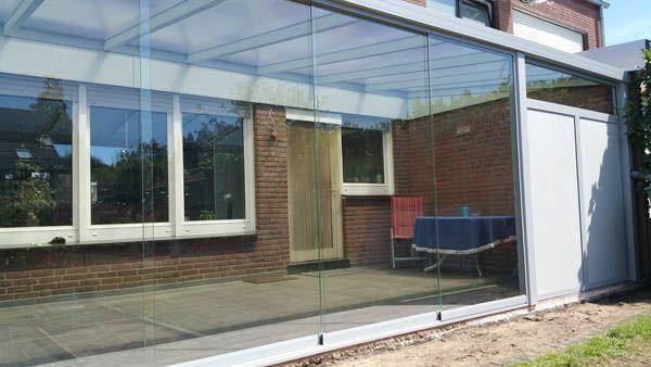 Verglaste Terrassenüberdachung mit Schiebetüren. Die Überdachung ist an ein Backsteinhaus angebaut. Im Inneren befinden sich ein Tisch und Stühle.