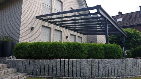 Moderne Terrasse mit dunklem Metalldach, Backsteinhaus und grünen Hecken.