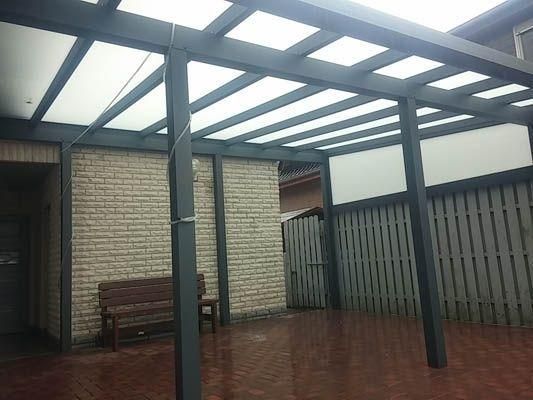 Pergola mit transparentem Dach, Ziegelmauer und Holzbank.