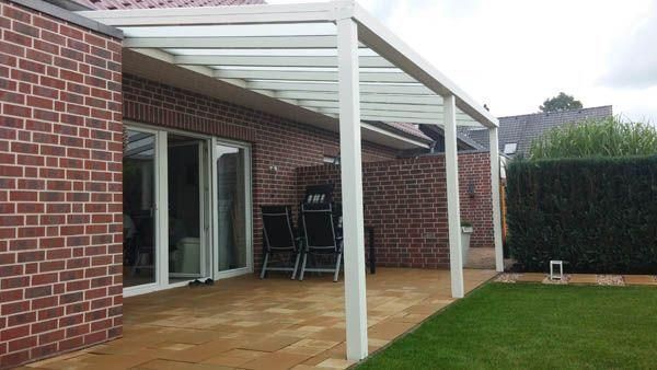 Eine weiß umrahmte Terrassenüberdachung mit Glasdach über einem Backsteinhaus bietet Blick auf einen Rasen.