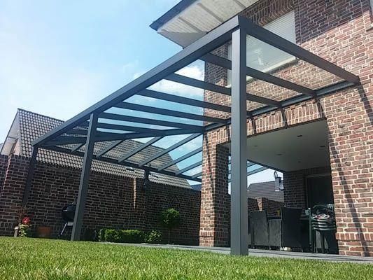 Eine Pergola mit transparentem Dach ist an ein Backsteinhaus angebaut. Sie bietet Blick auf eine Rasenfläche.