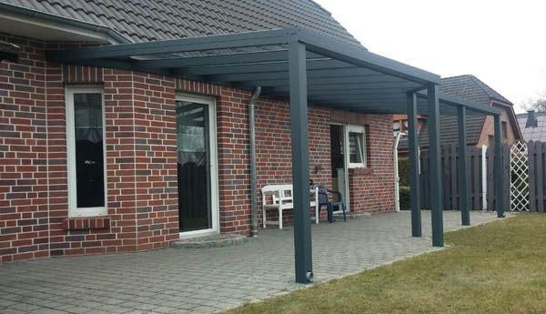 Von einem Backsteinhaus erstreckt sich eine graue Pergola und überspannt eine Terrasse.