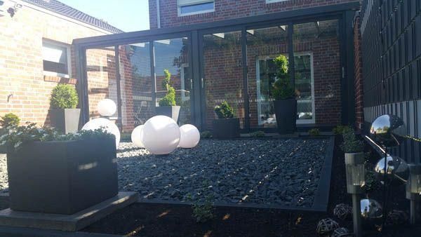 Terrasse im Freien mit dunkelgrauem Kies, Pflanzen und Glaswänden.