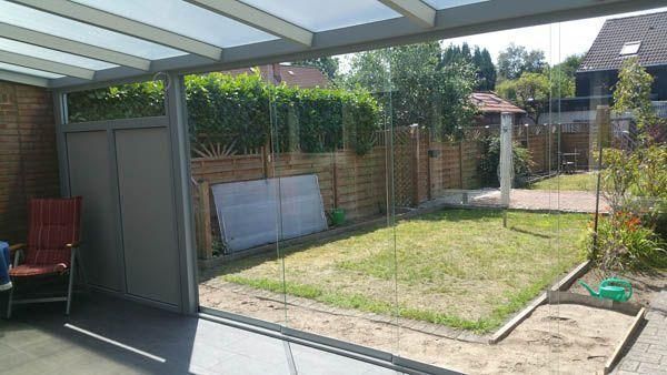 Verglaste Terrasse mit Blick auf einen Hinterhof mit Rasenfläche, umgeben von einem Holzzaun und Grünpflanzen.