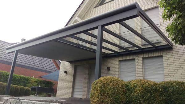 Graue Metallmarkise über dem Eingang eines Backsteinhauses. Die Markise hat ein Glasdach und graue Säulen.