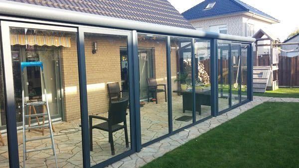 Ein verglaster Wintergarten, der an ein Backsteinhaus angebaut ist und über eine Terrasse, Stühle und einen üppigen grünen Rasen verfügt.