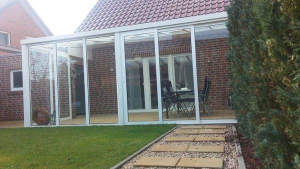 Ein verglaster Wintergarten, der an ein Backsteinhaus angebaut ist, mit einem Weg und einer Rasenfläche im Vordergrund.