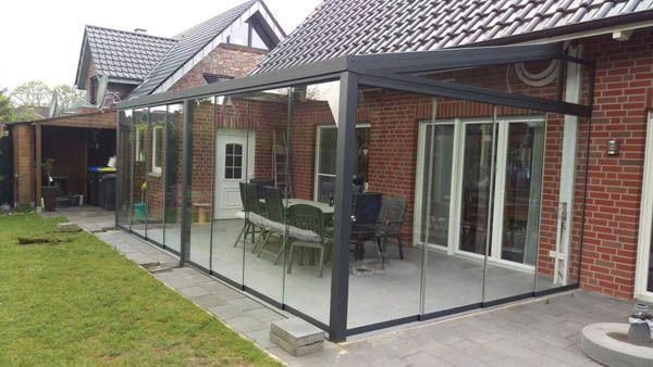 Verglaste Terrasse mit schwarzem Rahmen, die an ein Backsteinhaus angebaut ist. Ausgestattet mit einem Esstisch und Stühlen.