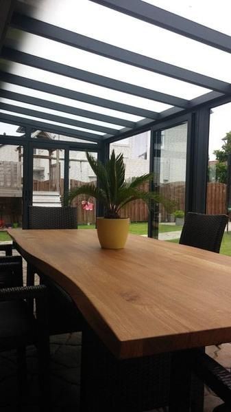 Essbereich im Freien mit Holztisch, Topfpflanze und Glasdach.