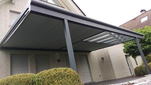 Eine graue Aluminiumpergola ist an ein helles Backsteinhaus angebaut und überspannt den Eingangsbereich.