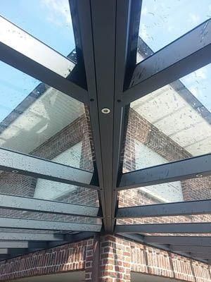 Glasdachkonstruktion über einem Backsteingebäude, blauer Himmel sichtbar.