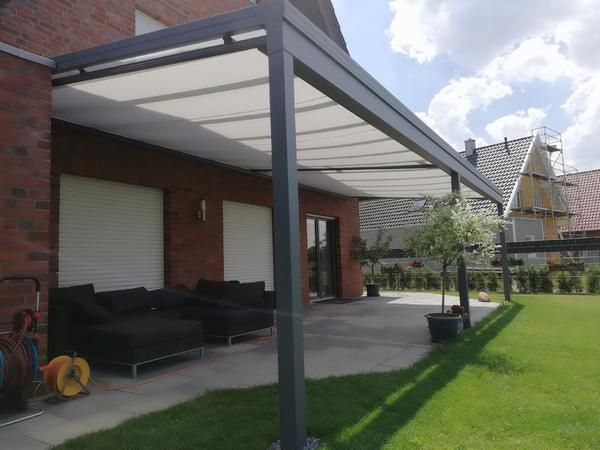 Pergola über einer Terrasse mit schwarzen Möbeln, an ein Backsteinhaus angebaut.