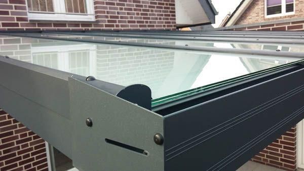 Nahaufnahme eines grau-schwarzen Gebäudes mit Glasdach; im Hintergrund ist ein Backsteingebäude zu sehen.