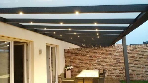 Terrasse mit modernem Pergola-Dach, Einbaustrahlern und Backsteinmauer. Darunter befinden sich Esstisch und Stühle.