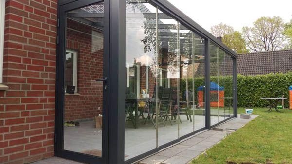 Ein verglaster Wintergarten, der an ein Backsteinhaus angebaut ist und auf einen Hof mit Tisch und Spielgerüst blickt.