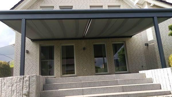 Graues Terrassendach überspannt die Stufen zu einem Backsteinhaus mit Glastüren.