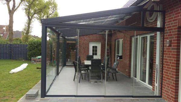 Verglaste Terrasse mit Esstisch und Stühlen, an ein Backsteinhaus angebaut. Mit Blick auf einen Garten.
