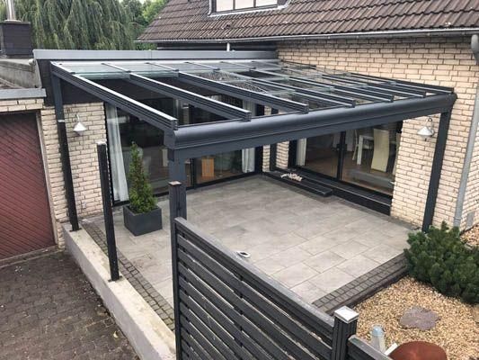 Eine mit grauem Rahmen versehene Glasterrasse ist an ein Backsteinhaus mit gefliester Terrasse angebaut.