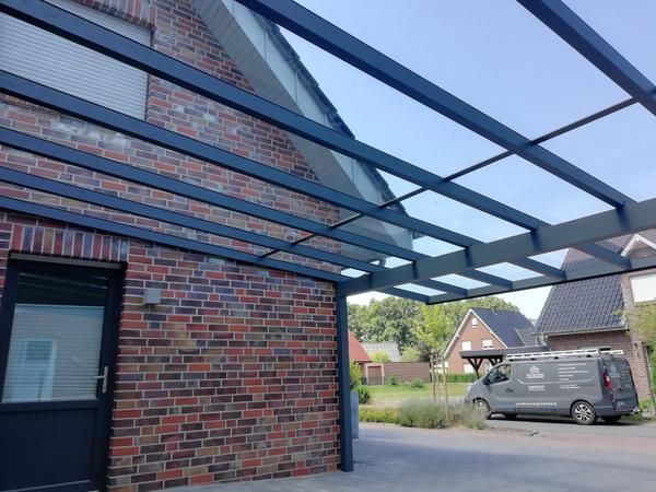 Ein moderner Carport mit transparentem Dach über einem Backsteinhaus und der dazugehörigen Einfahrt. Auf der Einfahrt steht ein Lieferwagen.