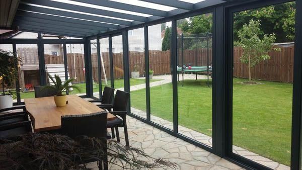 Wintergarten mit Glaswänden, Gartentisch und Stühlen mit Blick auf einen grünen Hof, ein Trampolin und Bäume.