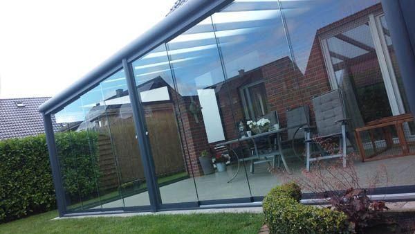 Ein verglaster Wintergarten, der an ein Backsteinhaus angebaut ist und den umliegenden Garten sowie das Innere des Hauses widerspiegelt.