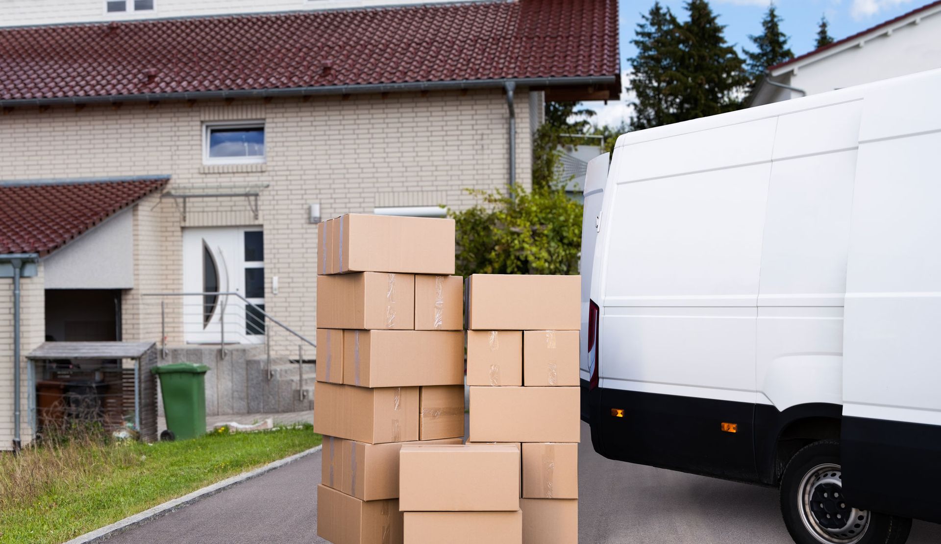 Eine vierköpfige Familie lächelt und sitzt auf dem Boden, umgeben von Umzugskartons, einem Laptop und einem Fußball.