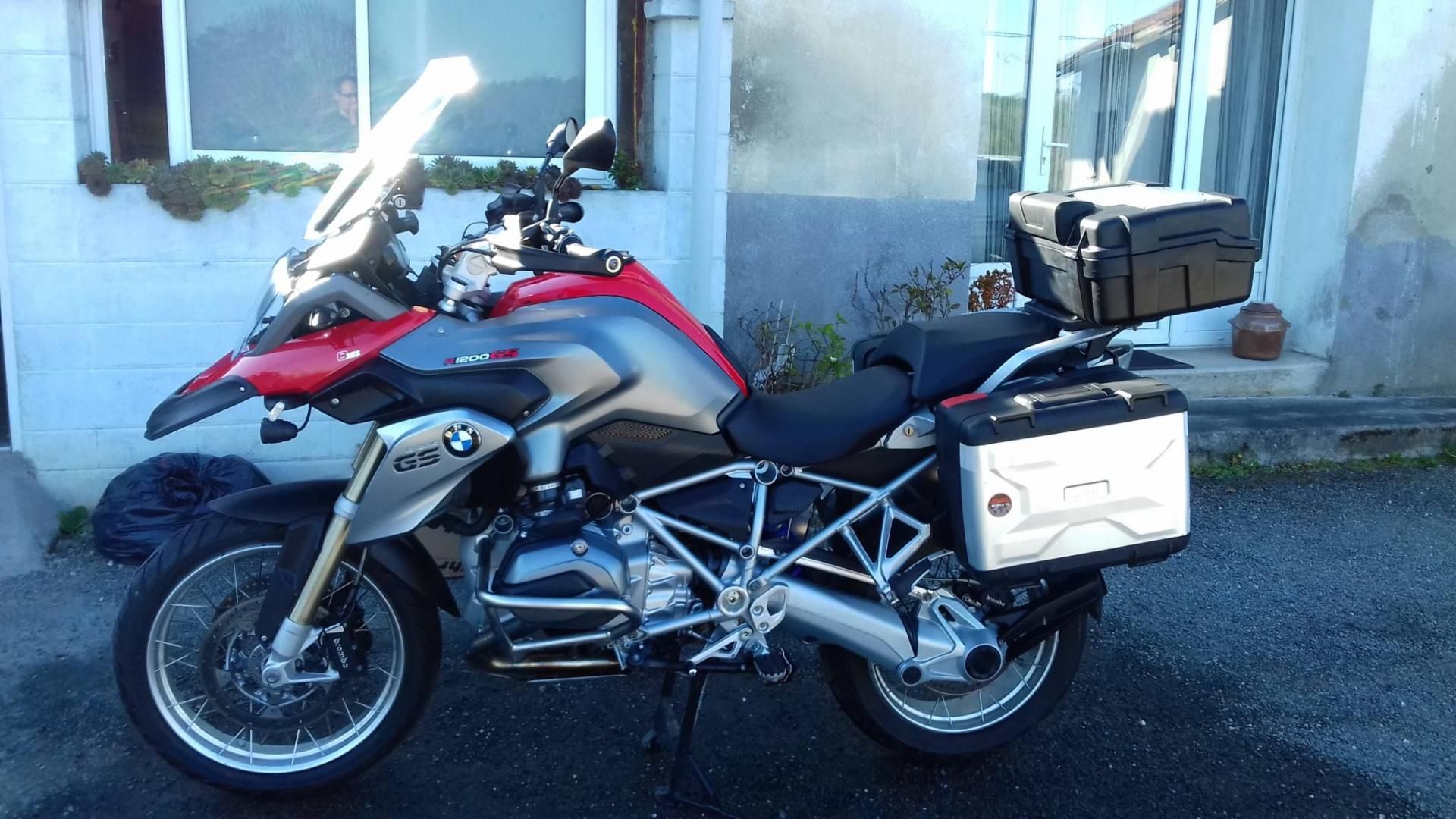 Moto de tourisme rouge et argent garée sur le trottoir à côté d’un bâtiment, avec des valises latérales