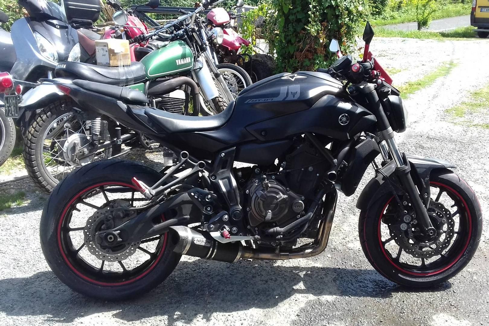 Moto sportive noire garée sur un chemin de gravier, à côté d’autres motos, en plein jour