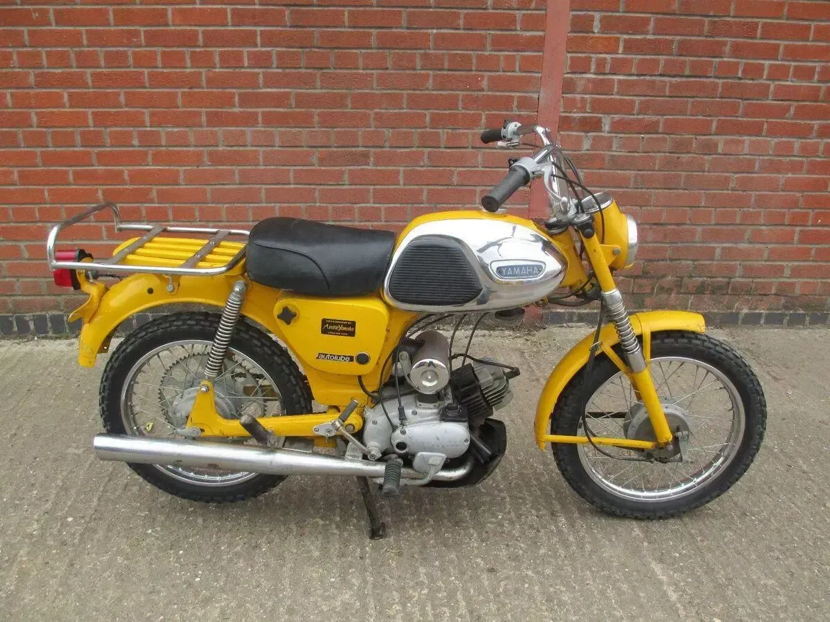 Moto vintage jaune garée contre un mur de briques rouges.