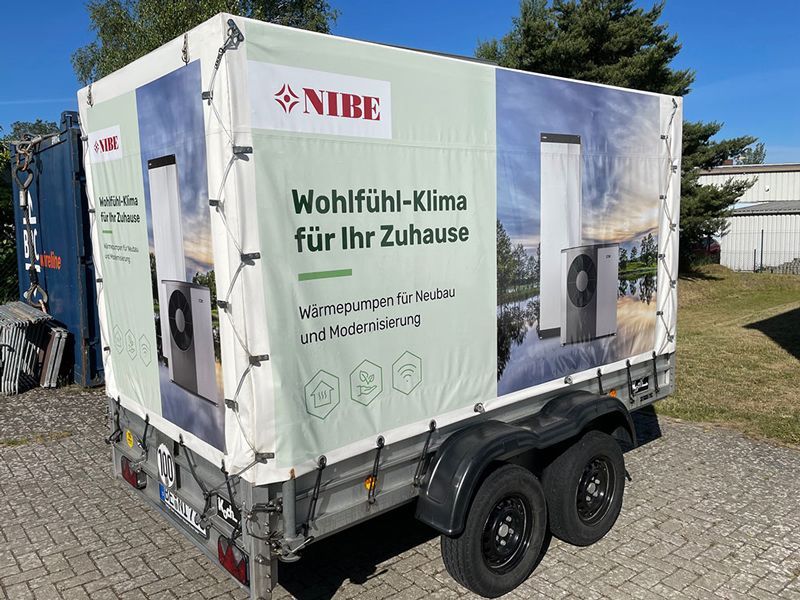 Am Straßenrand parkt ein Anhänger mit einer großen Werbung an der Seite.