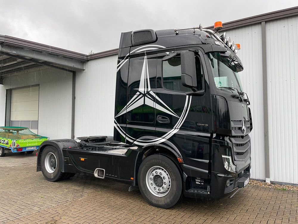 Vor einem Gebäude parkt ein schwarzer Mercedes-Truck.