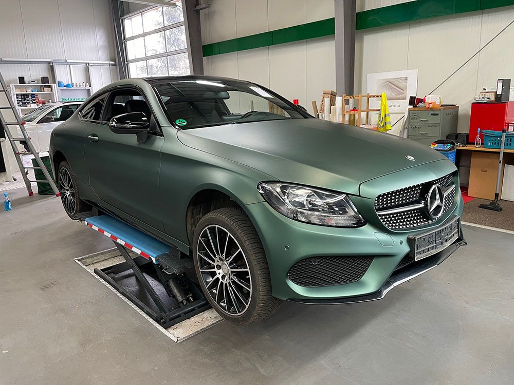 Ein grünes Mercedes C-Klasse Coupé steht auf einer Hebebühne in einer Garage.
