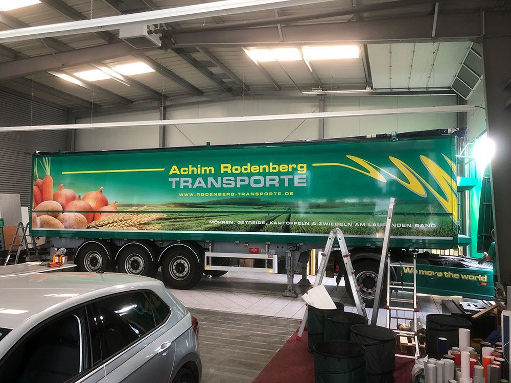 Ein grüner Lastwagen steht in einer Garage neben einem Auto.