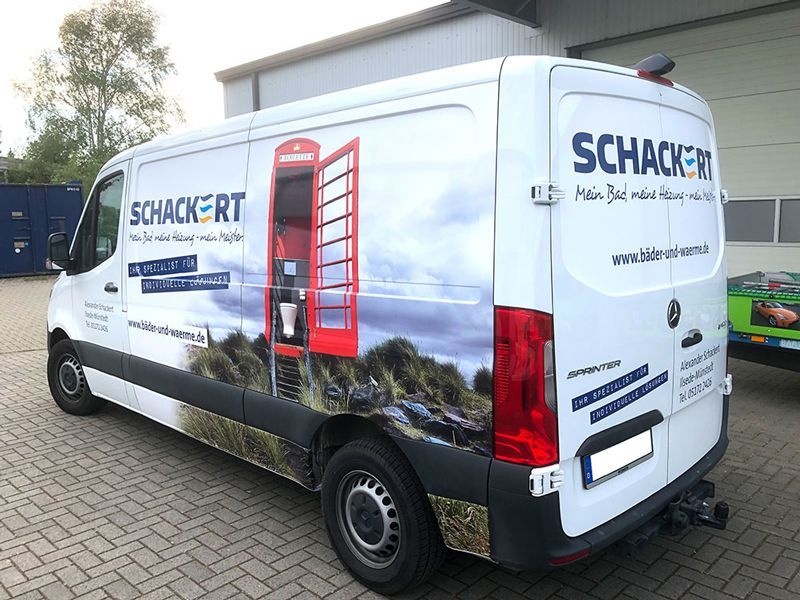 Auf einem Parkplatz steht ein weißer Lieferwagen mit einer roten Telefonzelle an der Seite.