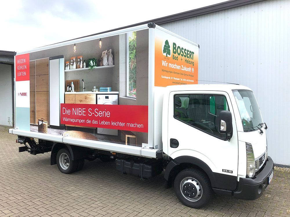 Ein weißer Lastwagen mit einem roten Schild an der Seite steht vor einem Gebäude.