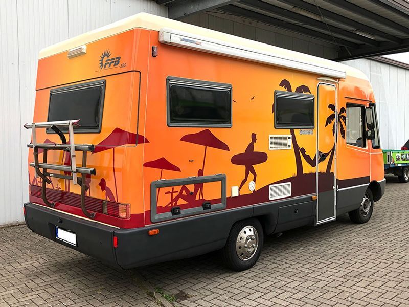 Auf einem Parkplatz steht ein buntes Wohnmobil.