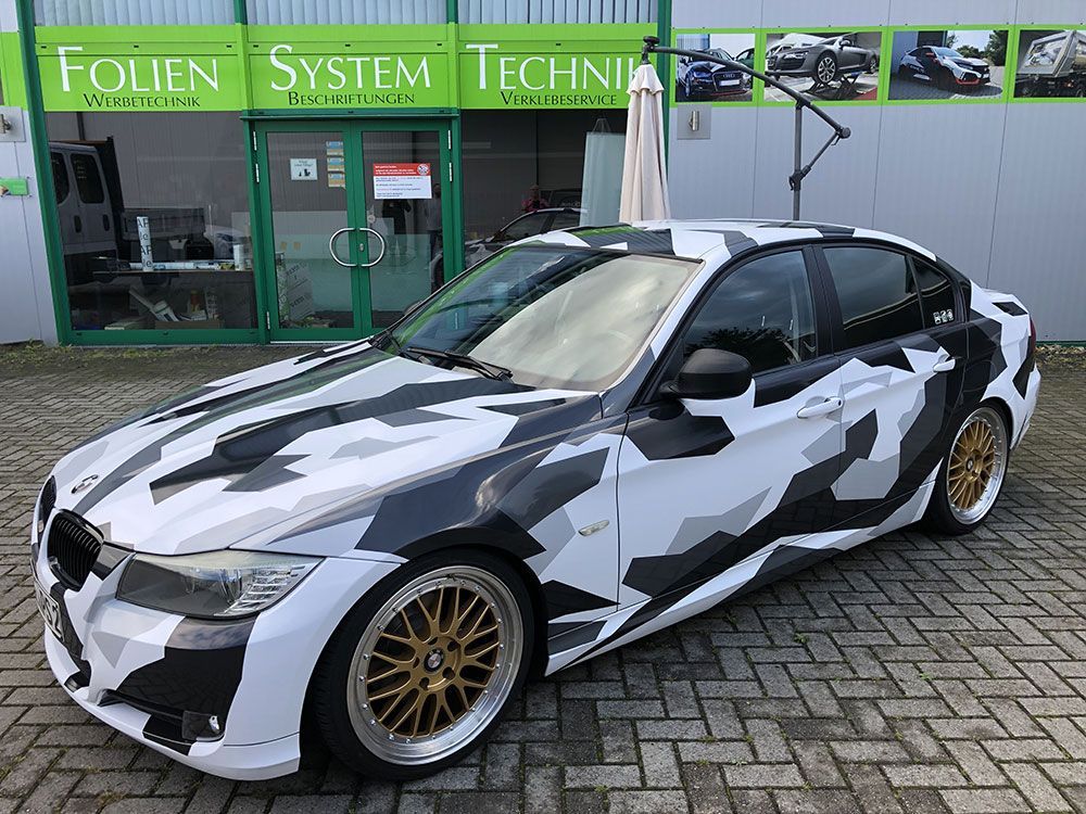 Vor einem Gebäude parkt ein schwarz-weiß getarntes Auto.