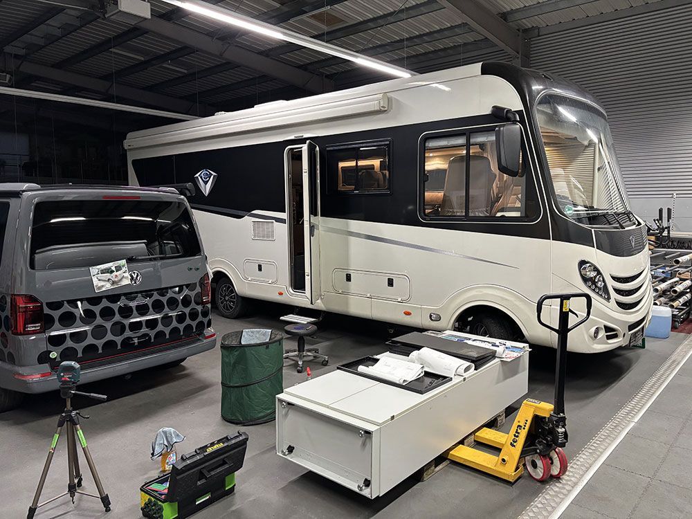 Ein großes Wohnmobil steht in einer Garage neben einem Lieferwagen.